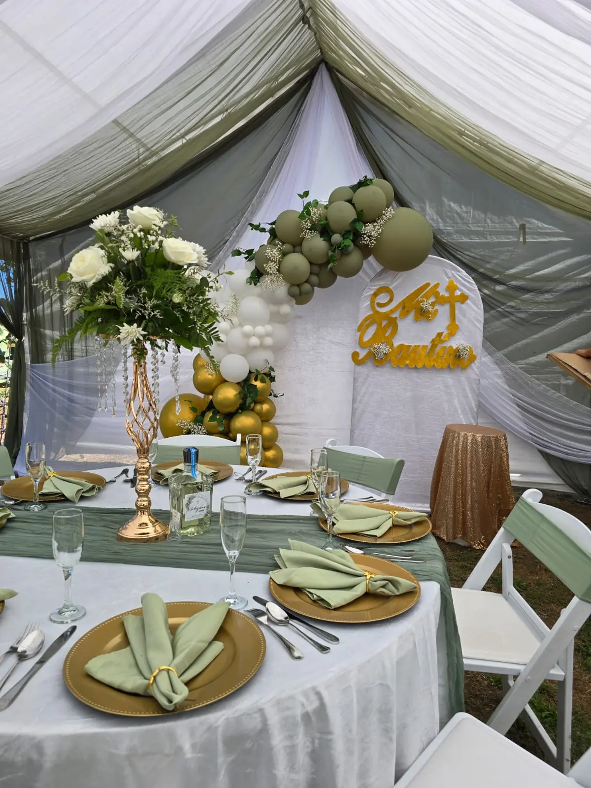 Sage and white tent setup with balloon arch backdrop and gold place settings