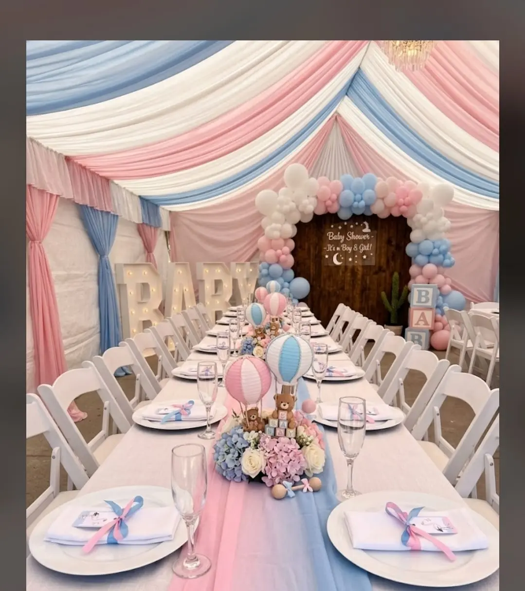 Pastel pink and blue baby shower tent with draped ceiling, balloon arch and long set table
