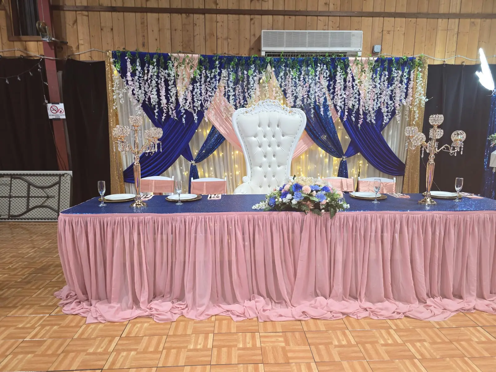Head table with royal blue and blush draped backdrop, hanging florals and a white throne chair