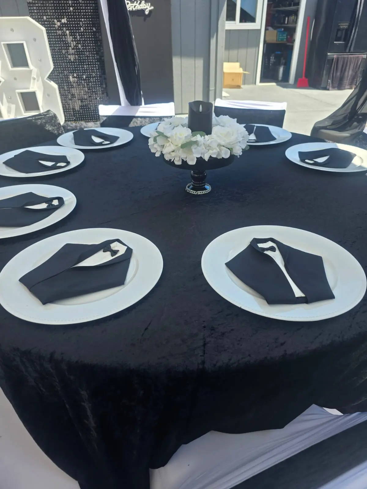 Round table with black velvet linen, white plates and tuxedo folded napkins
