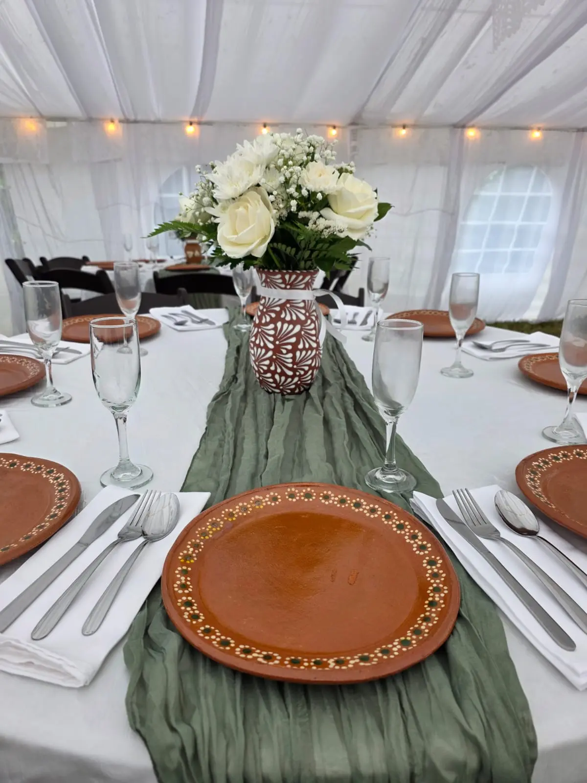 Round table with white linen, sage runner, clay plates and floral centerpiece