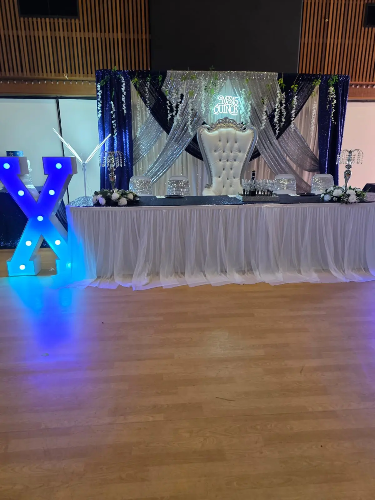 Blue quinceañera head table with sequined drapes and a Mis 15 neon sign
