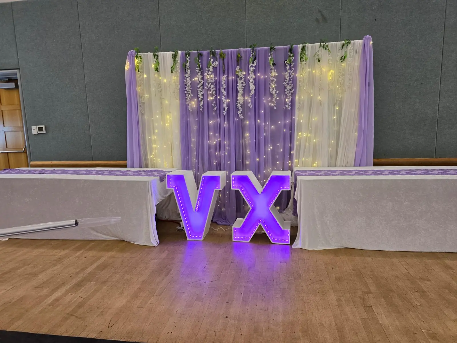 Purple and ivory draped backdrop with fairy lights and lit VX marquee letters