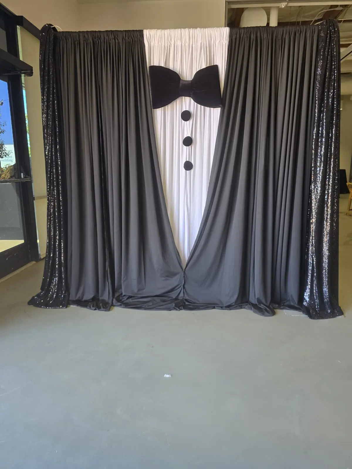 Tuxedo themed backdrop with black drapes, white panel, bow tie and buttons