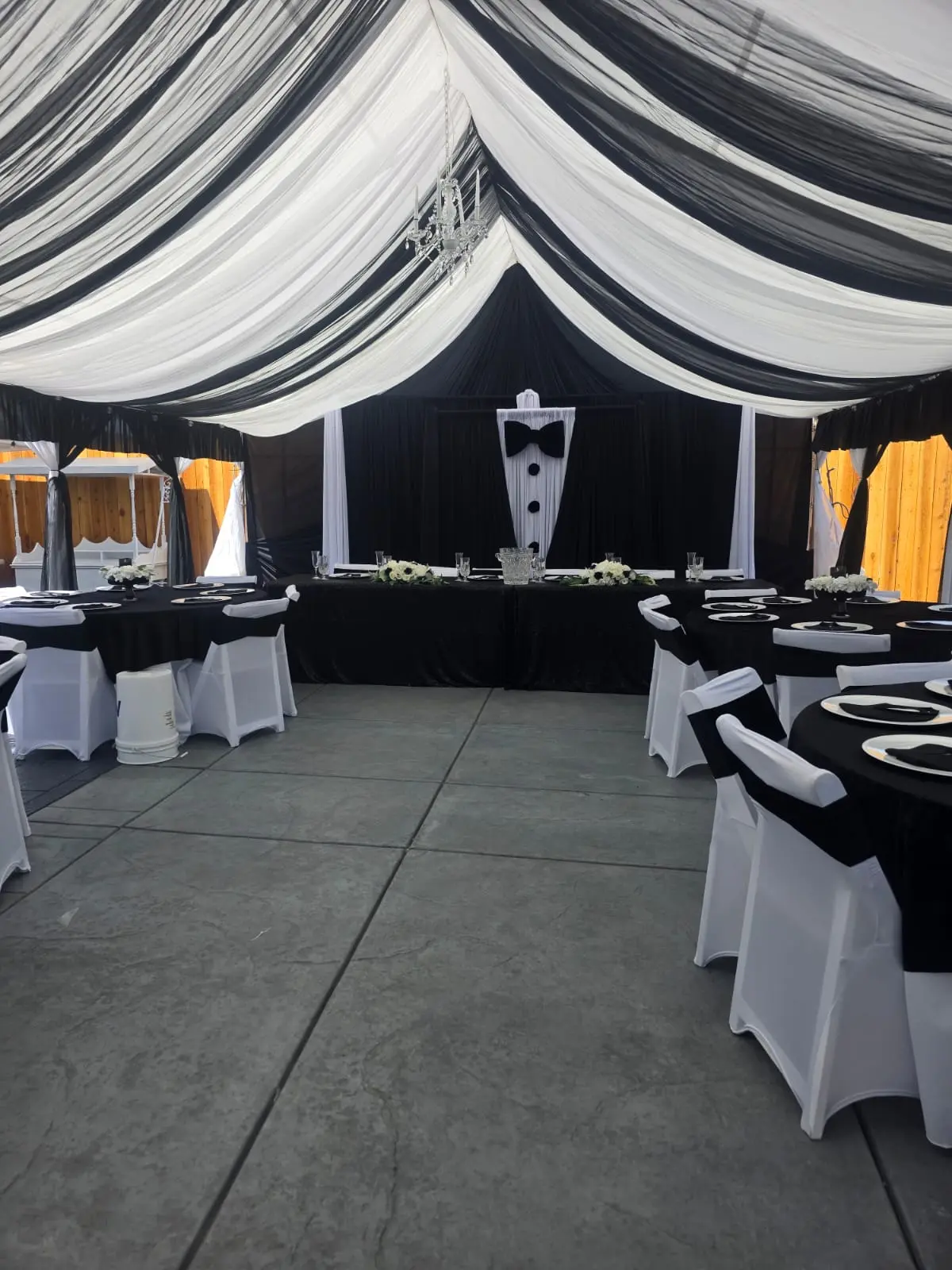 Tent with black and white ceiling draping, tuxedo backdrop and black linen tables