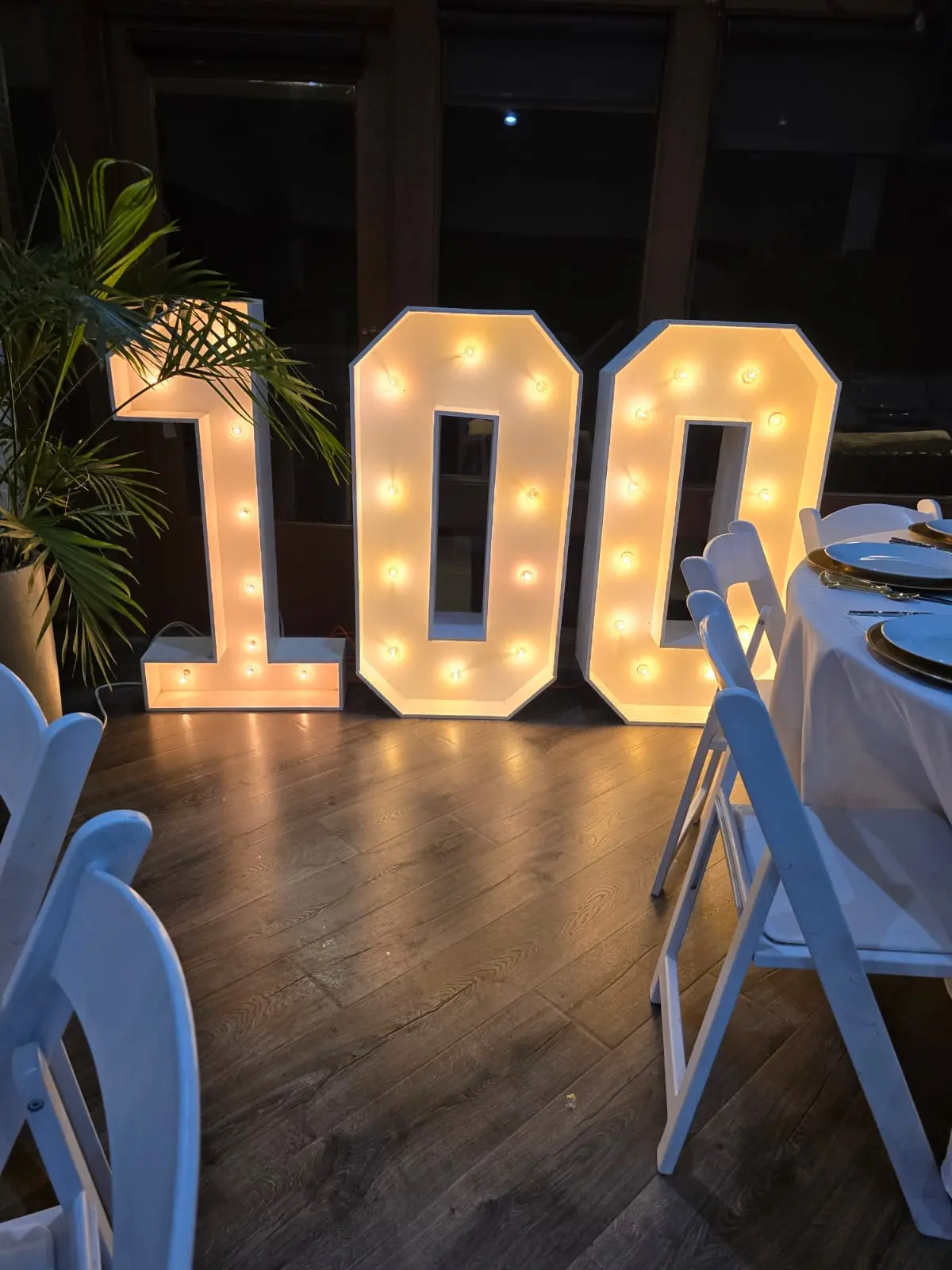 Illuminated marquee numbers 100 beside a set table with white folding chairs