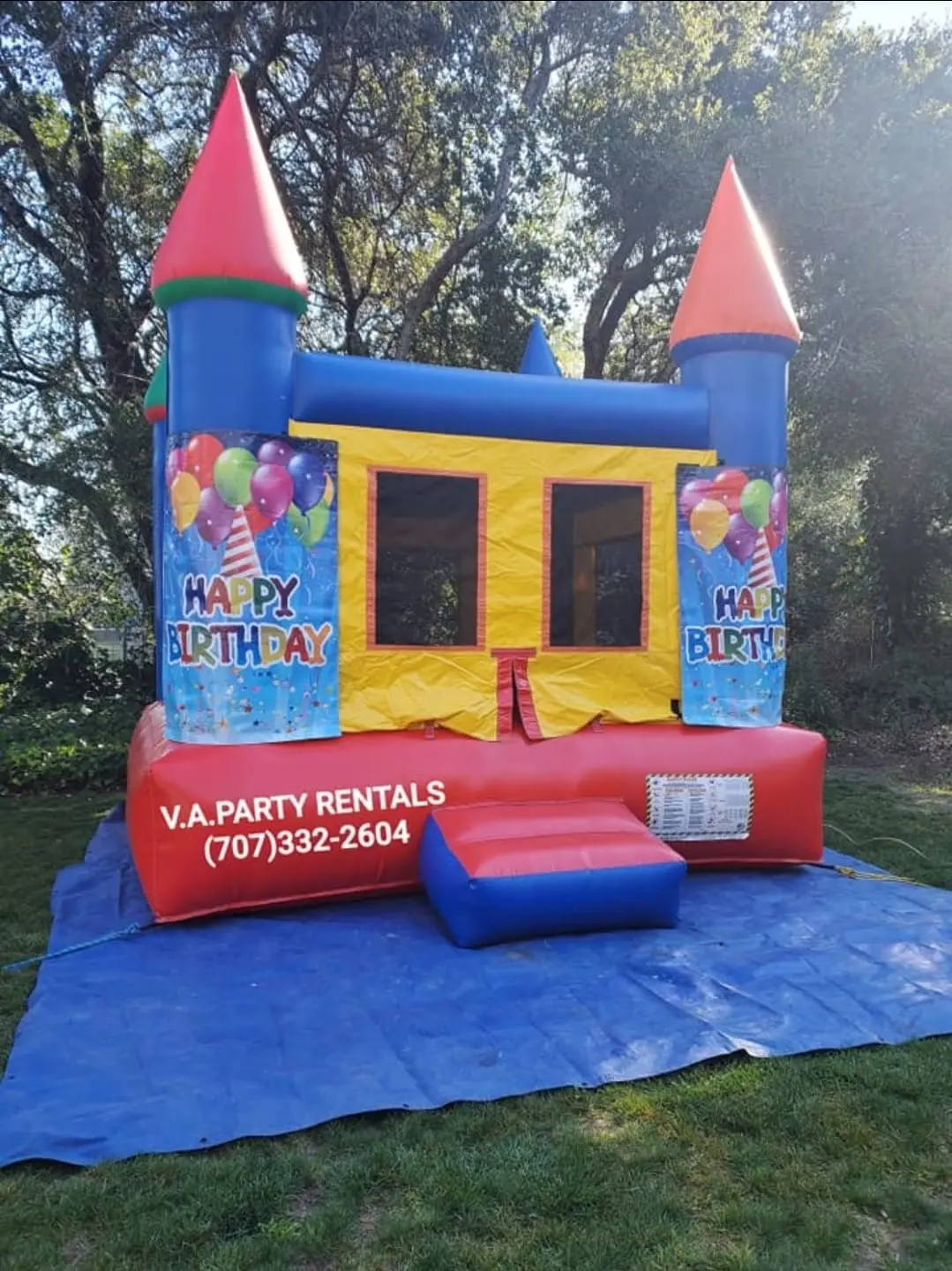 Birthday themed castle bounce house set up on a tarp over grass