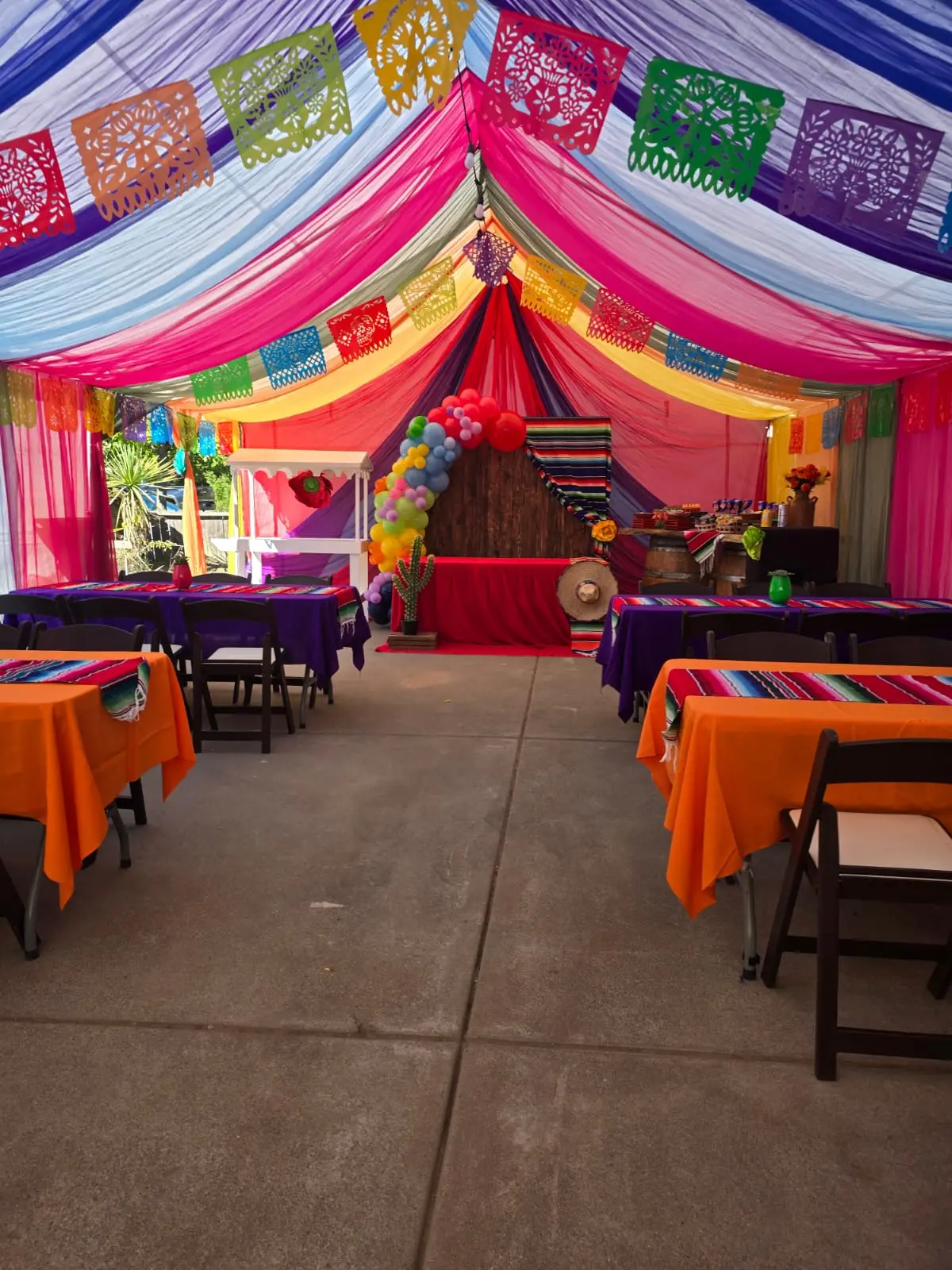Indoor fiesta setup with papel picado banners and orange tablecloths