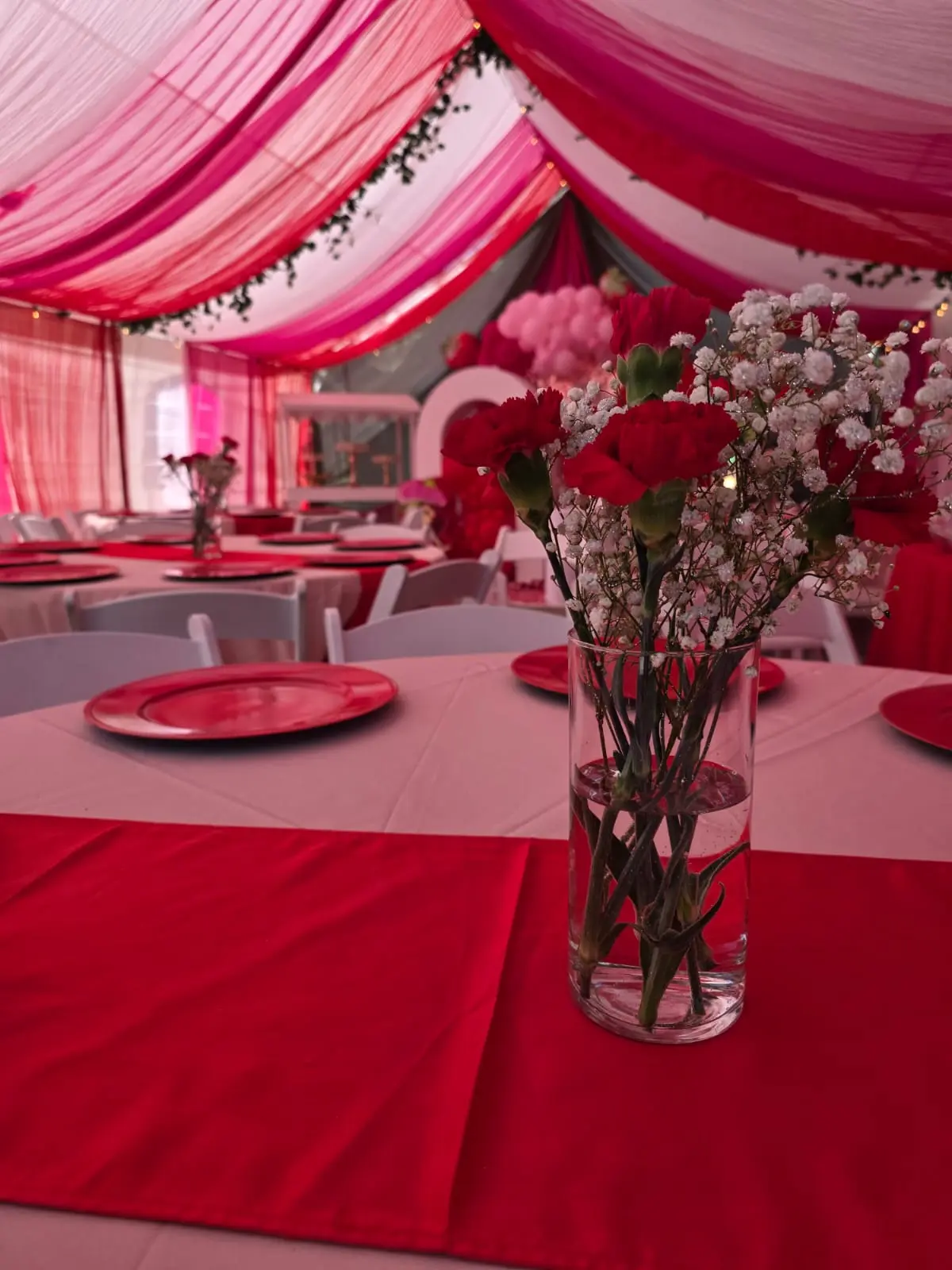 Event area under a pink draped tent with white tables and red runners