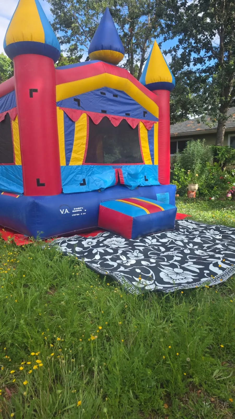 Red, yellow and blue castle bounce house set up on a lawn with an entry mat