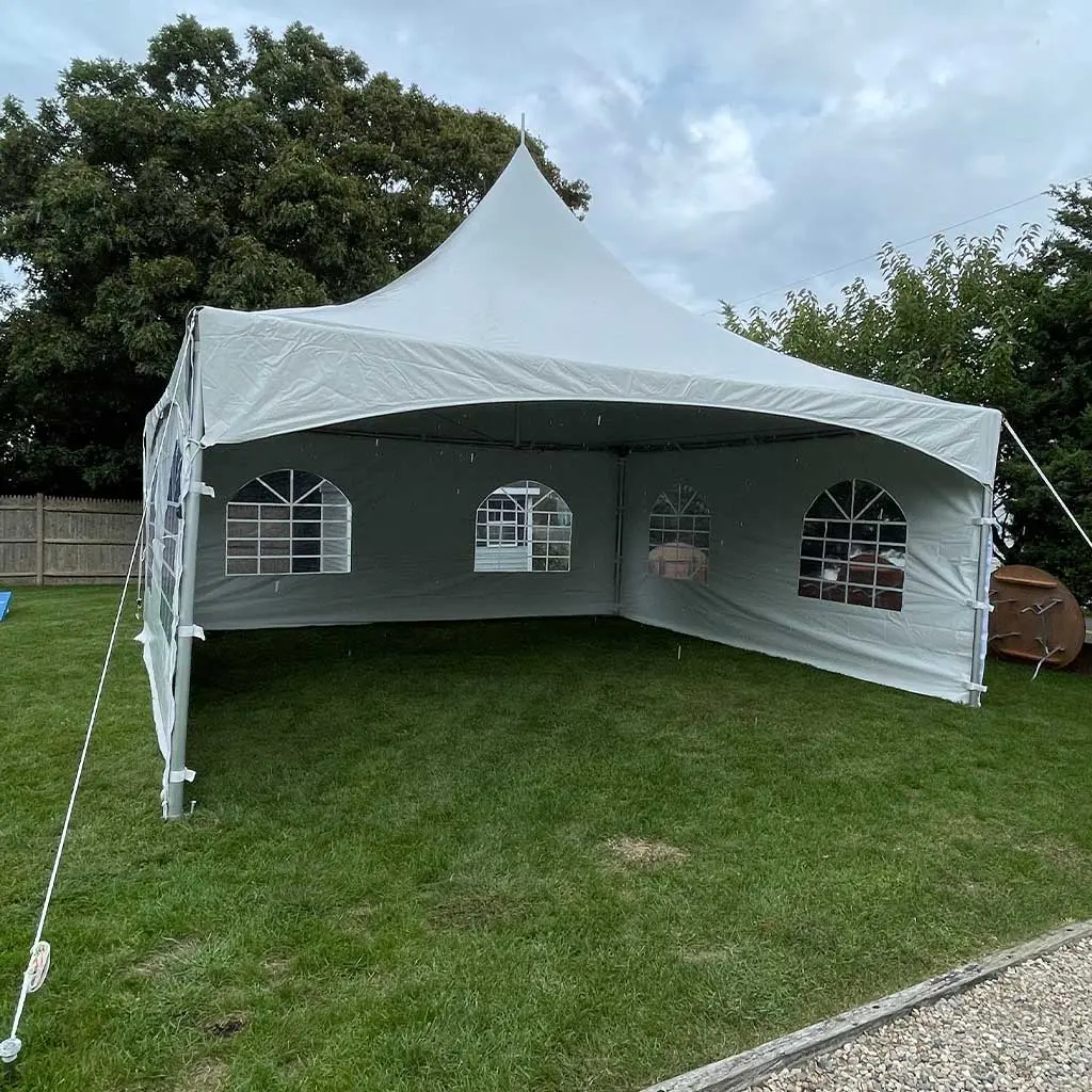 White frame tent with peaked roof and arched window sidewalls set up on grass