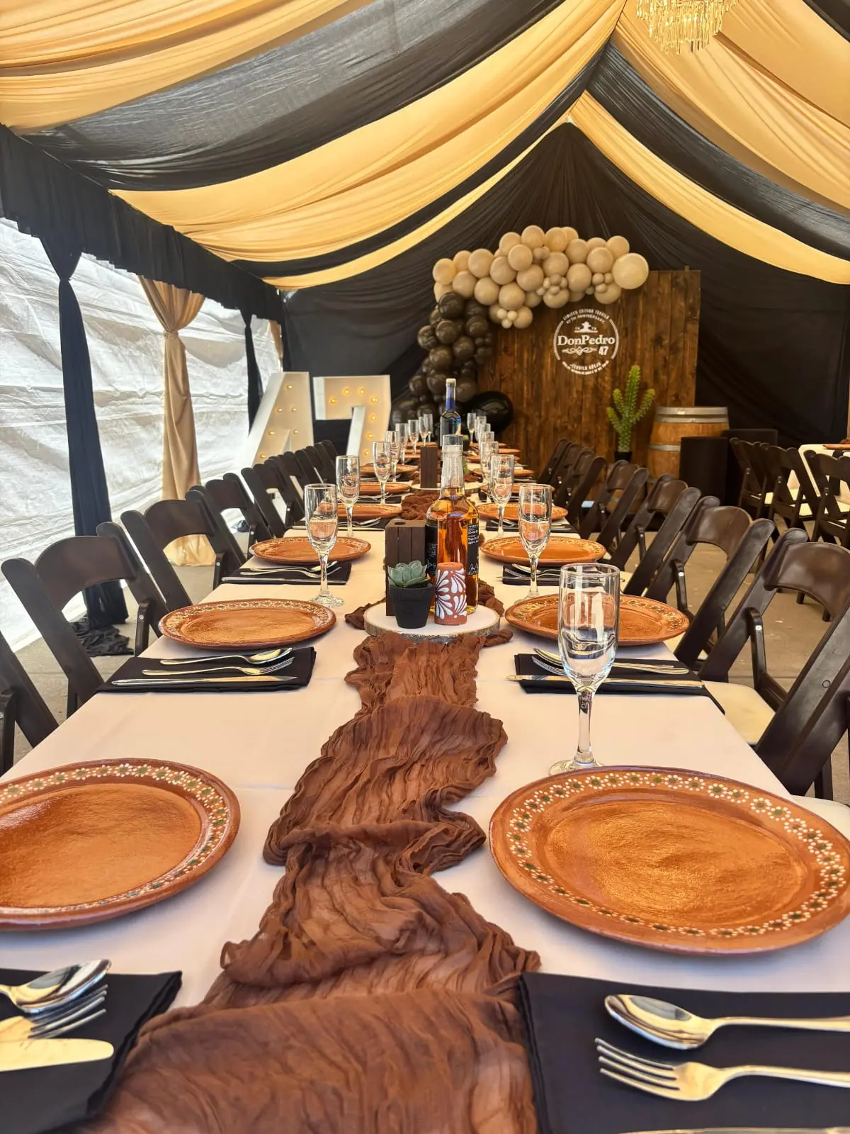 Place settings with clay chargers and a rust runner under black and gold tent draping