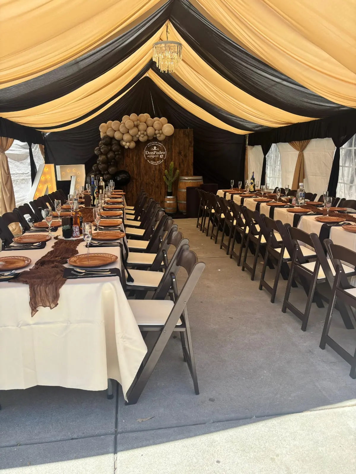 Tent with black and gold draping, long banquet tables and dark folding chairs