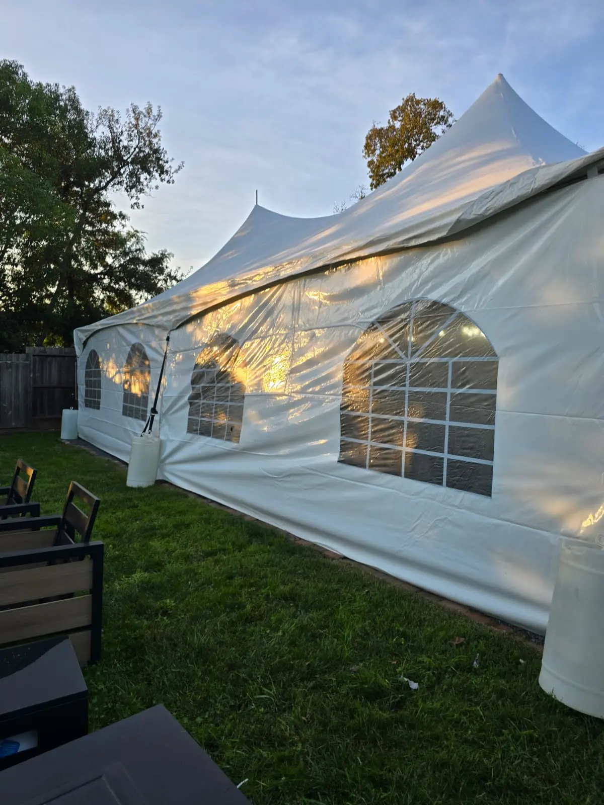 White frame tent set up on a lawn with arched window sidewalls at sunset