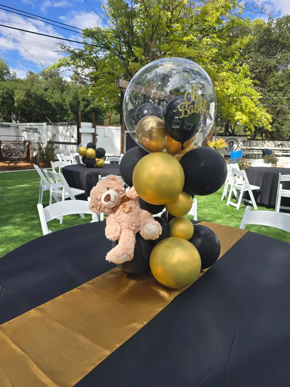 Black and gold balloon centerpiece with teddy bear on a table with gold runner