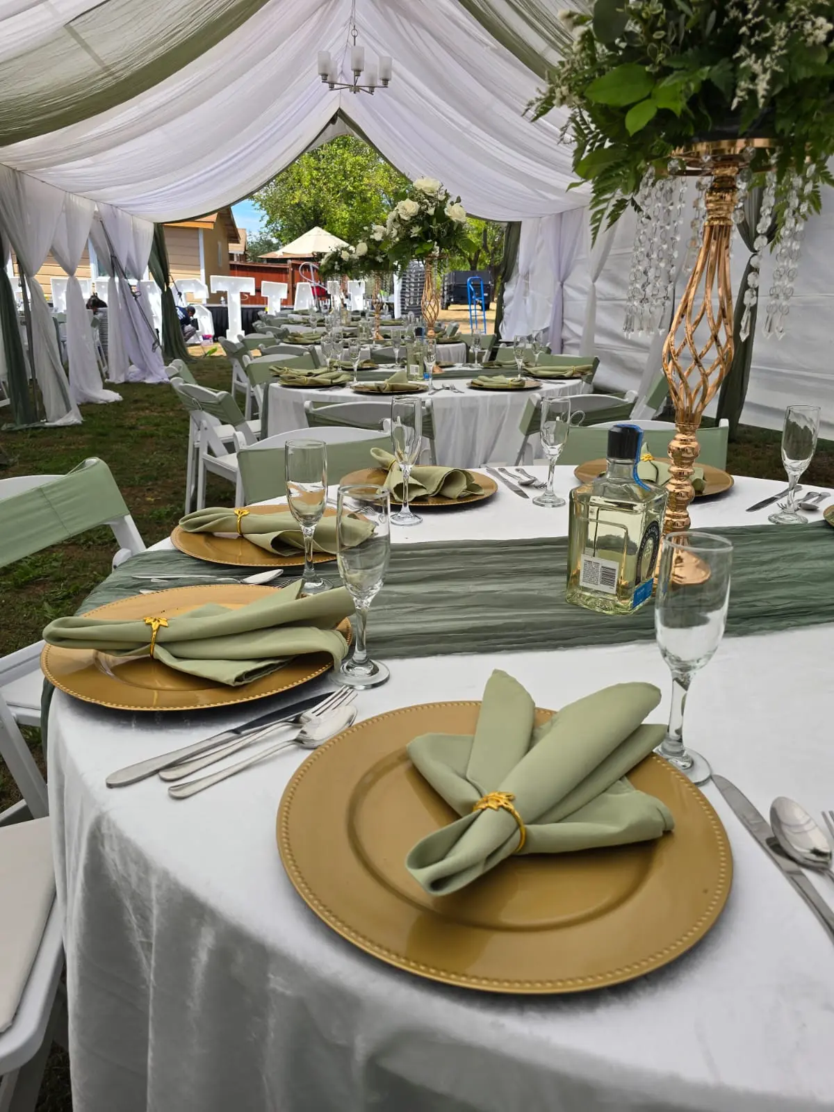 Round and rectangular tables with sage napkins and gold chargers under white tent draping