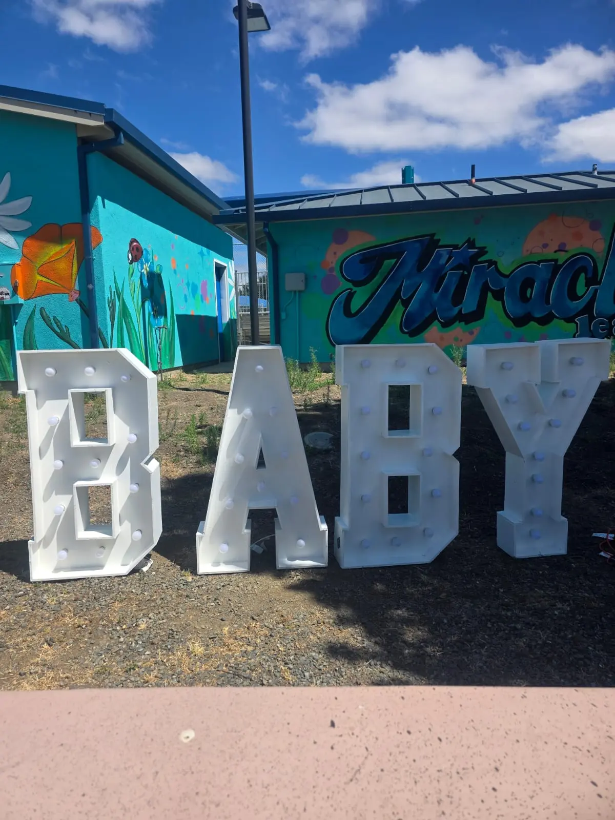 Large illuminated marquee letters spelling BABY set up outdoors for a celebration