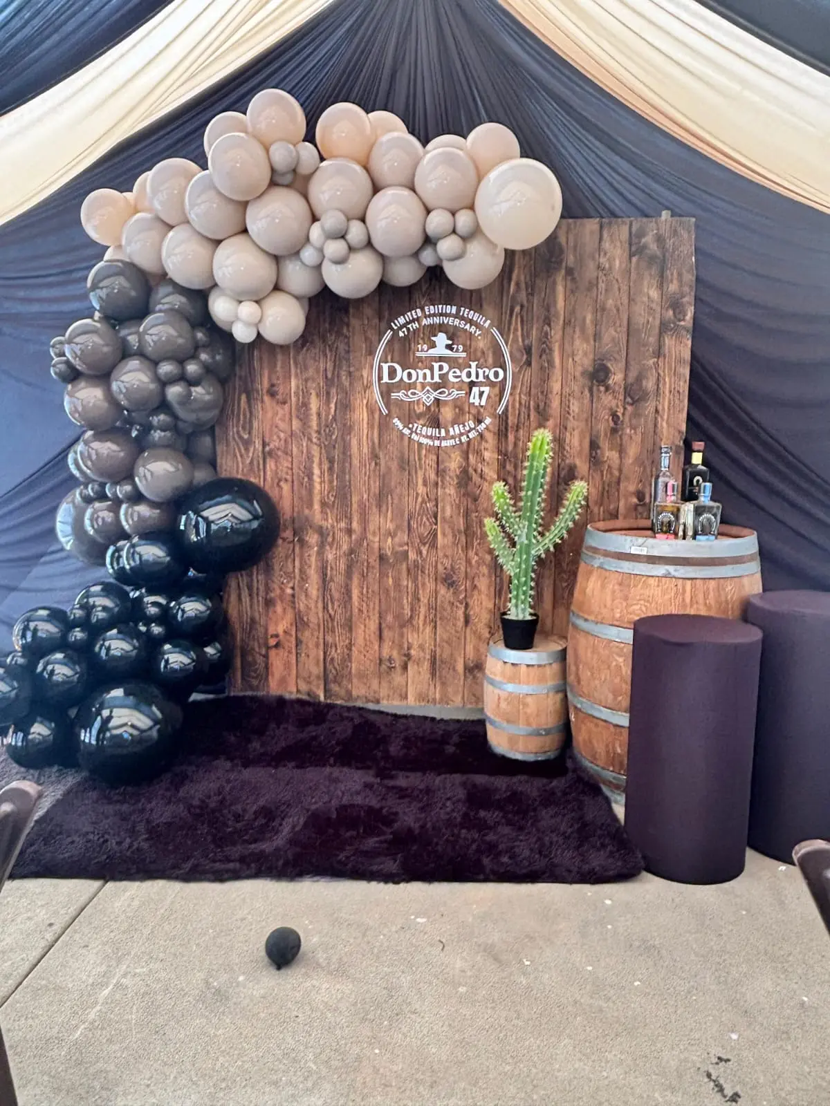 Rustic backdrop with wood panel, neutral and black balloon garland, barrels and cactus