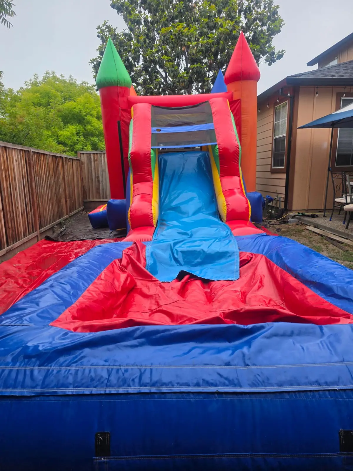 Bounce house with a tall blue water slide and splash landing in a backyard